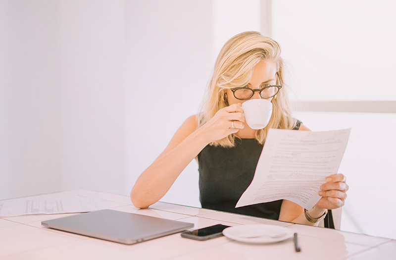 Donna bionda che legge un documento mentre beve un caffè