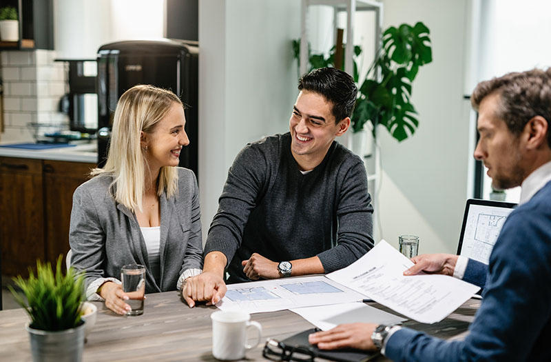 Due acquirenti felici siedono al tavolo con un consulente immobiliare e firmano i documenti contrattuali.
