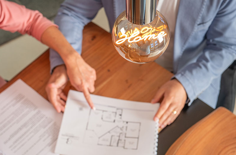 Zwei Personen besprechen gemeinsam Grundriss und Vertragsunterlagen bei einem Immobilienverkauf in vertrauensvoller Atmosphäre.