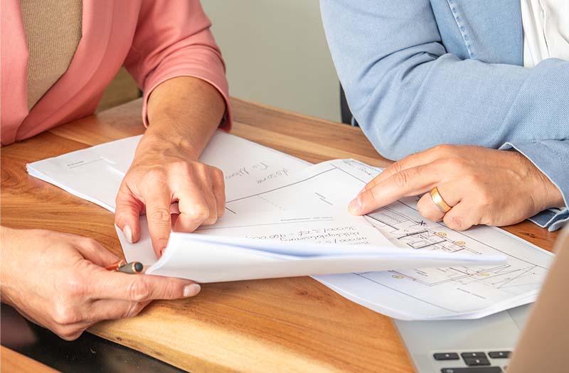 Due persone analizzano insieme documenti e planimetrie – un’immagine che rappresenta l’attenta consultazione dell’estratto del registro fondiario prima dell’acquisto di un immobile.